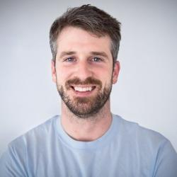 Bradley Farquhar has short sandy brown hair and a beard. He's wearing a grey tshirt and standing in front of a plain grey backdrop