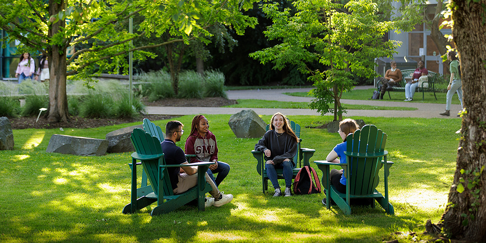 Students sitting in comfortable chairs among the trees on campus.