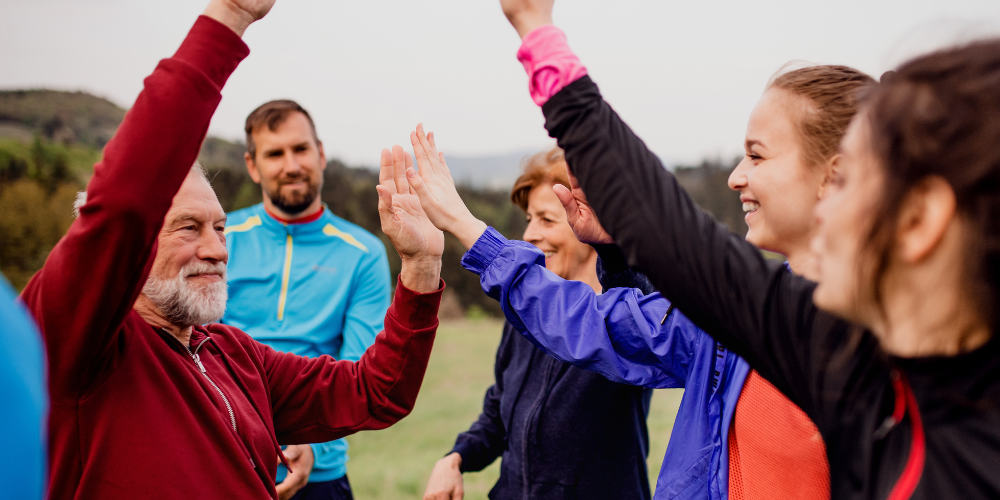 A group of people of various ages high five while doing an outdoor activity